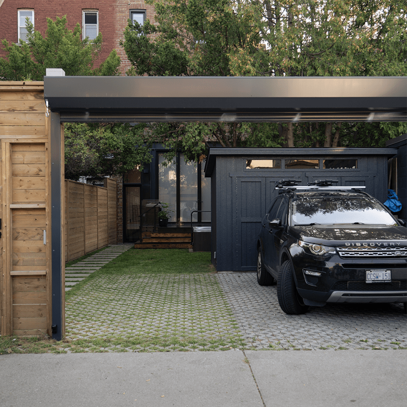 Modern house with brick exterior, spacious driveway, and parked SUV. Surrounded by lush greenery and wooden fencing, creating a cozy, urban retreat.